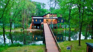 A house with a wooden deck leading to a dock over water, surrounded by trees. - All is Found Riverfront Cabin with Sauna (Broken Bow)