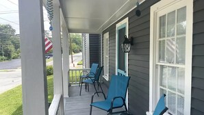 Eine Veranda mit blauen Stühlen und einem Tisch, einem weißen Geländer und einem Fenster mit weißen Fensterläden.
