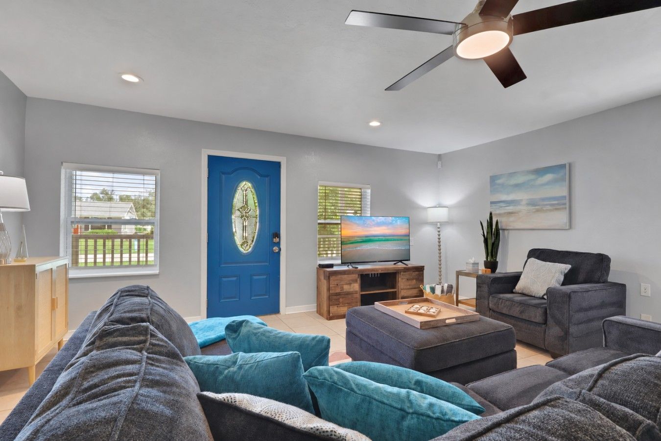A modern living room with a blue door, a flat-screen TV, and a ceiling fan.
