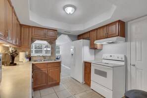 A kitchen with wooden cabinets, a white stove, and a refrigerator. - Home w/ Fenced Yard, Hot tub, Grill & 3 King Beds! (Sarasota)