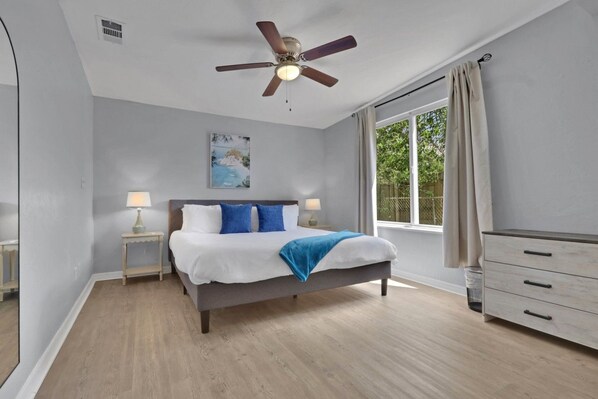 A bedroom with a bed, bedside tables, a ceiling fan, a window with curtains, and a dresser.