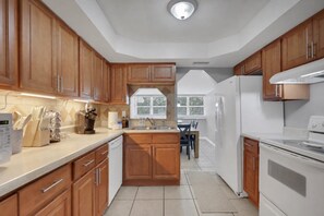 A modern kitchen with wooden cabinets, a central island, a refrigerator, and a stove. - Home w/ Fenced Yard, Hot tub, Grill & 3 King Beds! (Sarasota)