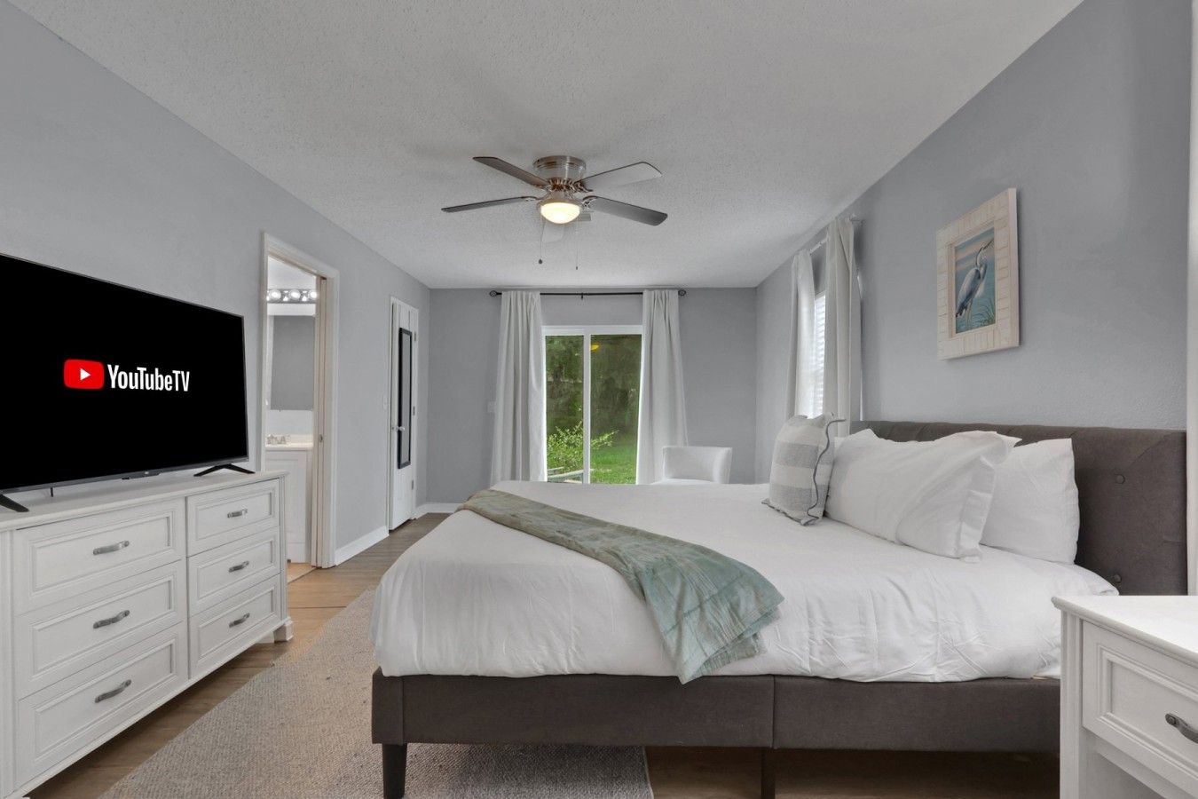 A bedroom with a bed, a TV, a ceiling fan, and a window with curtains.