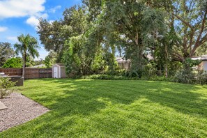 A well-maintained backyard with a lawn, a shed, and mature trees. - Home w/ Fenced Yard, Hot tub, Grill & 3 King Beds! (Sarasota)