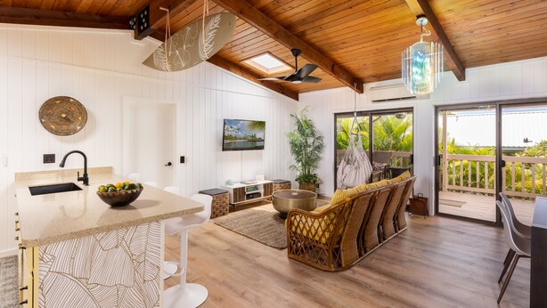 A spacious kitchen with a large island, a dining area with wicker furniture, and a balcony with a view of the outdoors.