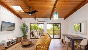 A spacious living area with a wooden ceiling, a large sofa, a dining table with chairs, and a view of the outdoors through large sliding glass doors.