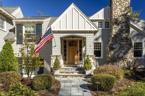 Une maison à deux étages avec une cheminée en pierre, un porche à l’avant et un drapeau.