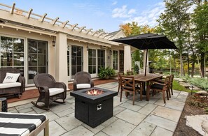 Une terrasse extérieure avec un foyer, des meubles en osier et une table à manger avec des chaises.