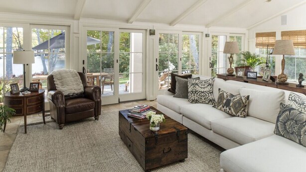 Amplia sala de estar con un sillón de cuero, un sofá y una mesa de centro. Amplias ventanas con vistas al exterior.