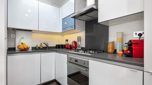 A modern kitchen with white cabinets, a stainless steel range hood, and a red coffee machine. - Farringdon/St Pancras penthouse (London)