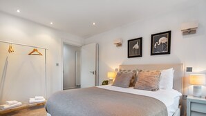 A modern bedroom with a large bed, bedside tables, a wardrobe, and two framed pictures on the wall. - Farringdon/St Pancras penthouse (London)