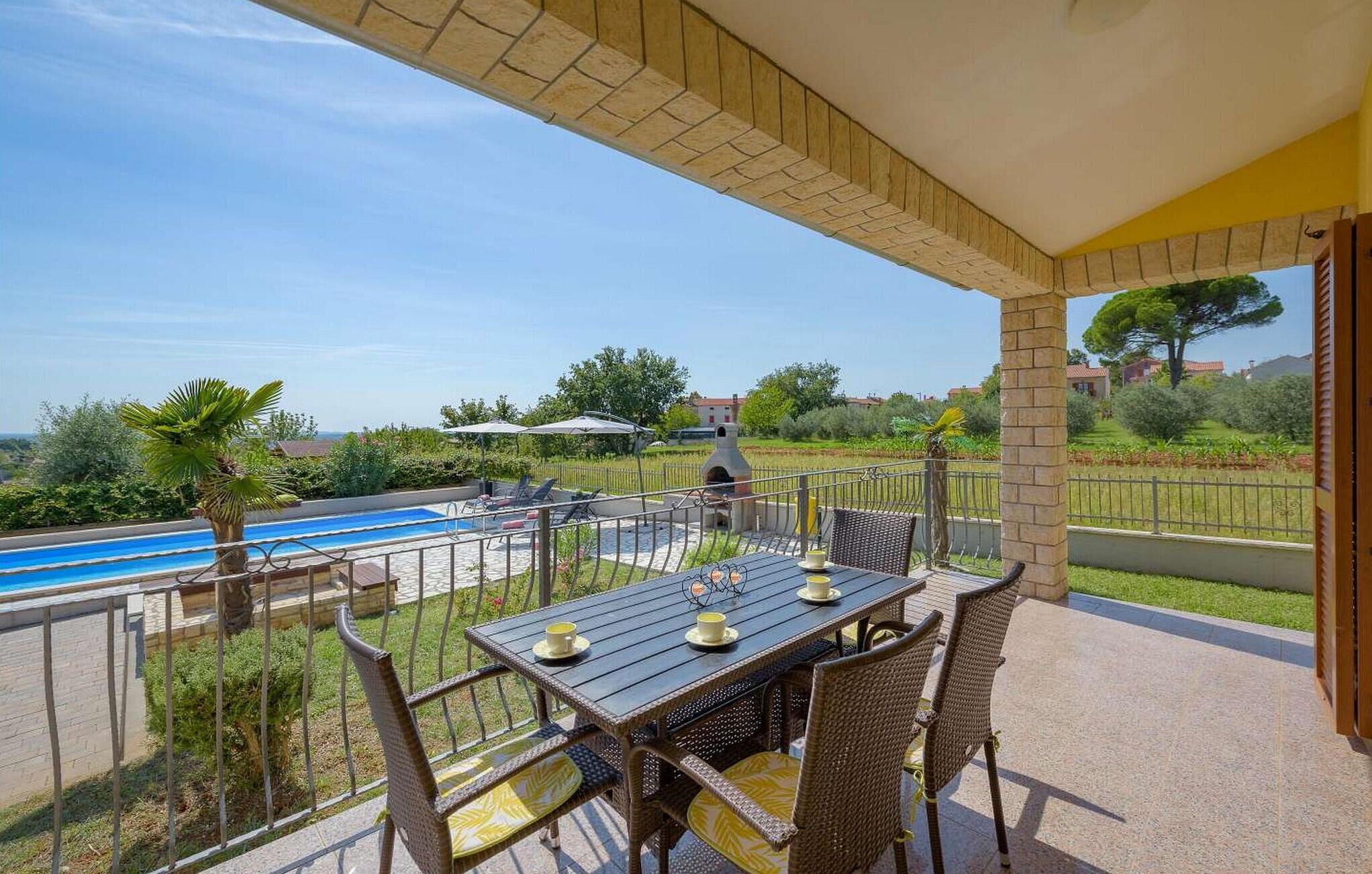 A covered outdoor area with a pool, a table with chairs, and a view of the surrounding landscape.