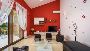 A modern living room with a red accent wall, a glass coffee table, black sofas, a TV, and a balcony with red curtains. - Stunning home in Kastelir-Labinci (Kastelir-Labinci)