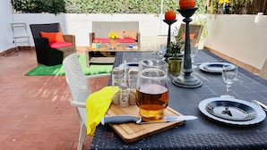 Un espace de restauration en plein air avec une table dressée pour deux personnes, comprenant des assiettes, des couverts et un verre contenant un liquide ambré.