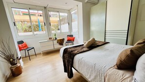 Une chambre moderne avec un lit, un bureau et une chaise. Une fenêtre offre une vue sur les bâtiments environnants.