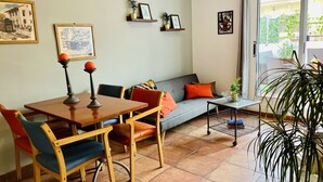 Un salon chaleureux avec une table à manger, des chaises, un canapé avec des coussins, une petite table d’appoint et une plante en pot.