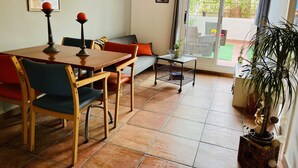 Un coin repas avec une table et des chaises en bois, une petite table d’appoint agrémentée d’une plante, et une porte-fenêtre coulissante donnant sur une terrasse extérieure.