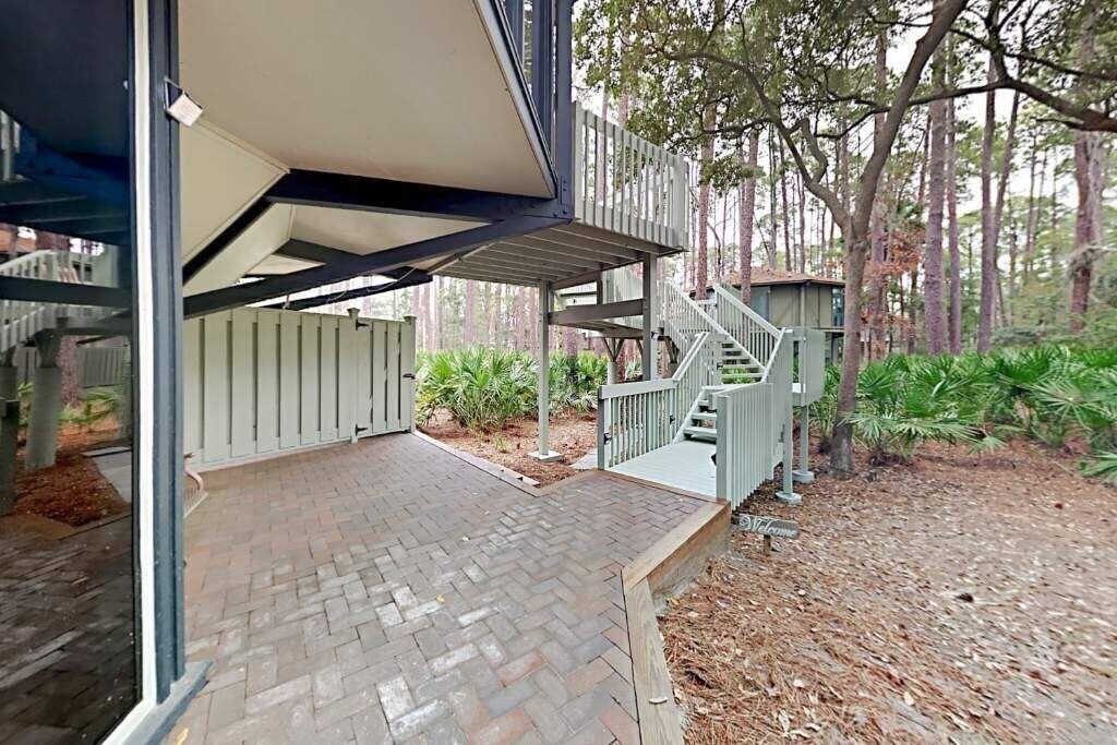 Un espace extérieur abrité comprenant une terrasse en briques, une plateforme en bois et un escalier menant à un bâtiment.