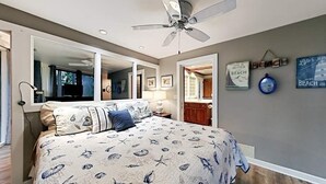 Quarto com cama, ventilador de teto e vista para o banheiro.