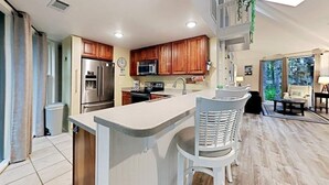 Uma cozinha moderna com armários de madeira, eletrodomésticos de aço inoxidável e um espaço bar com banquetas brancas.