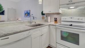 Une cuisine moderne avec des meubles blancs, un lave-vaisselle encastré, un évier en acier inoxydable et une cuisinière blanche.