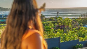 A person overlooking a coastal view with a lighthouse, greenery, and parked cars.