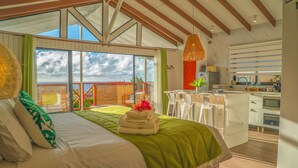 A bedroom with a large window, a bed with green bedding, and a view of the outside.