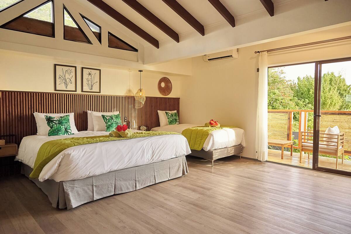 Una camera da letto con due letti, pavimento in legno, un'ampia finestra e un balcone.
