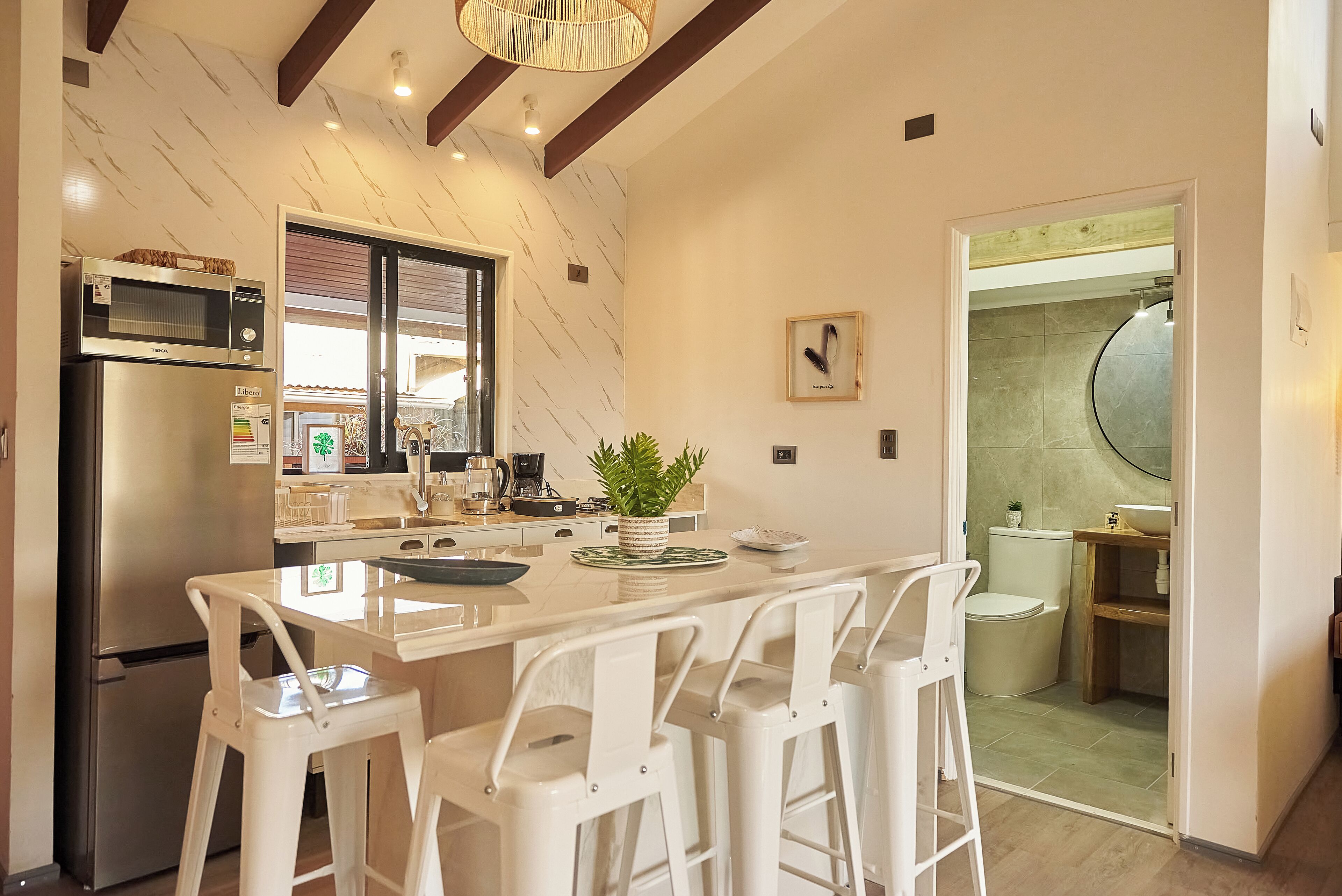 A modern kitchen with a central island, bar stools, a refrigerator, a microwave, and a sink.