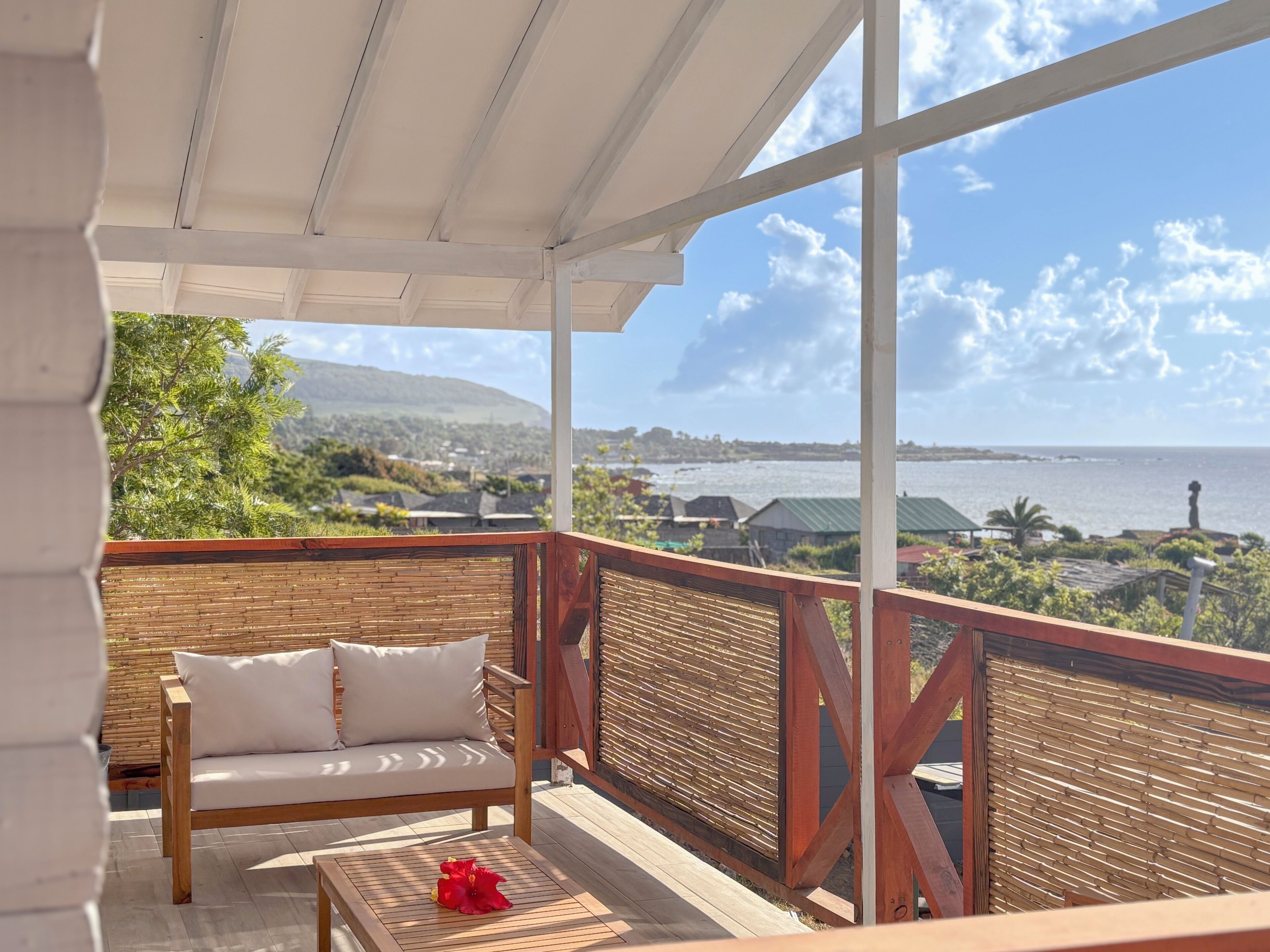 A wooden deck with a sofa and a table, overlooking a coastal view with mountains and a body of water.