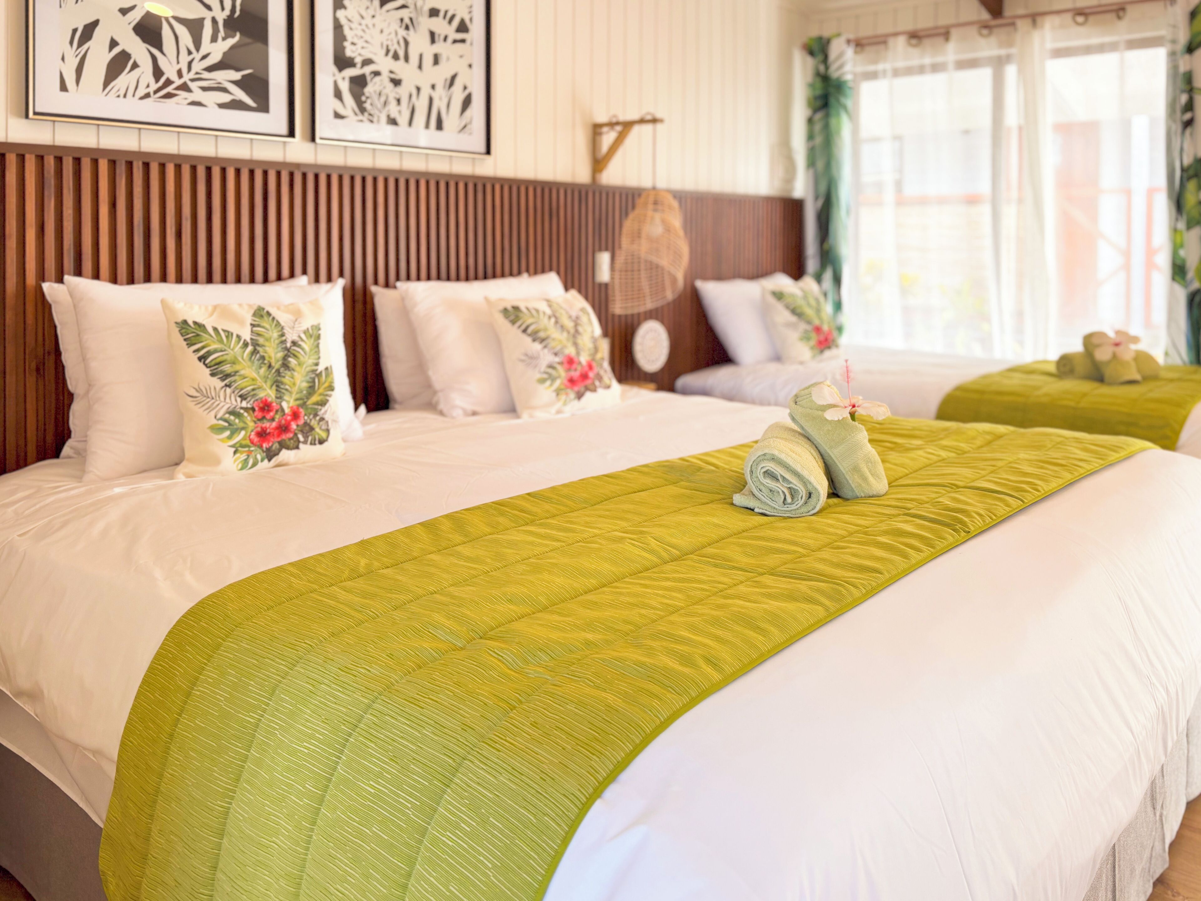 A hotel room with a large bed, a wooden headboard, and a green quilt.