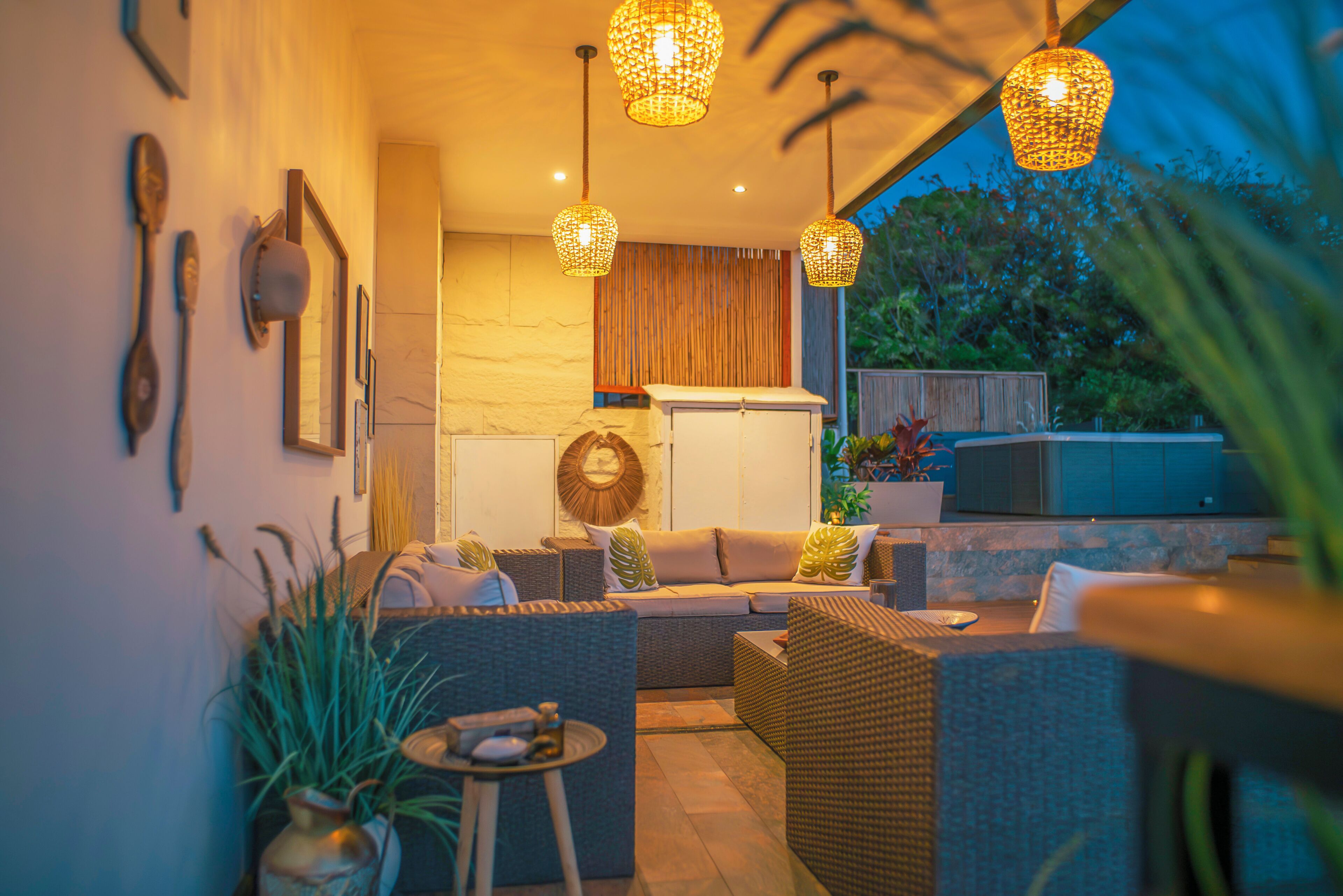 A modern outdoor living space with wicker furniture, pendant lighting, and a view of the outdoors.