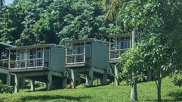 Un edificio de diseño moderno, elevado sobre pilotes, rodeado de abundante vegetación.