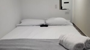 Habitación de hotel con cama, manta, toalla enrollada, unidad de aire acondicionado y espejo.