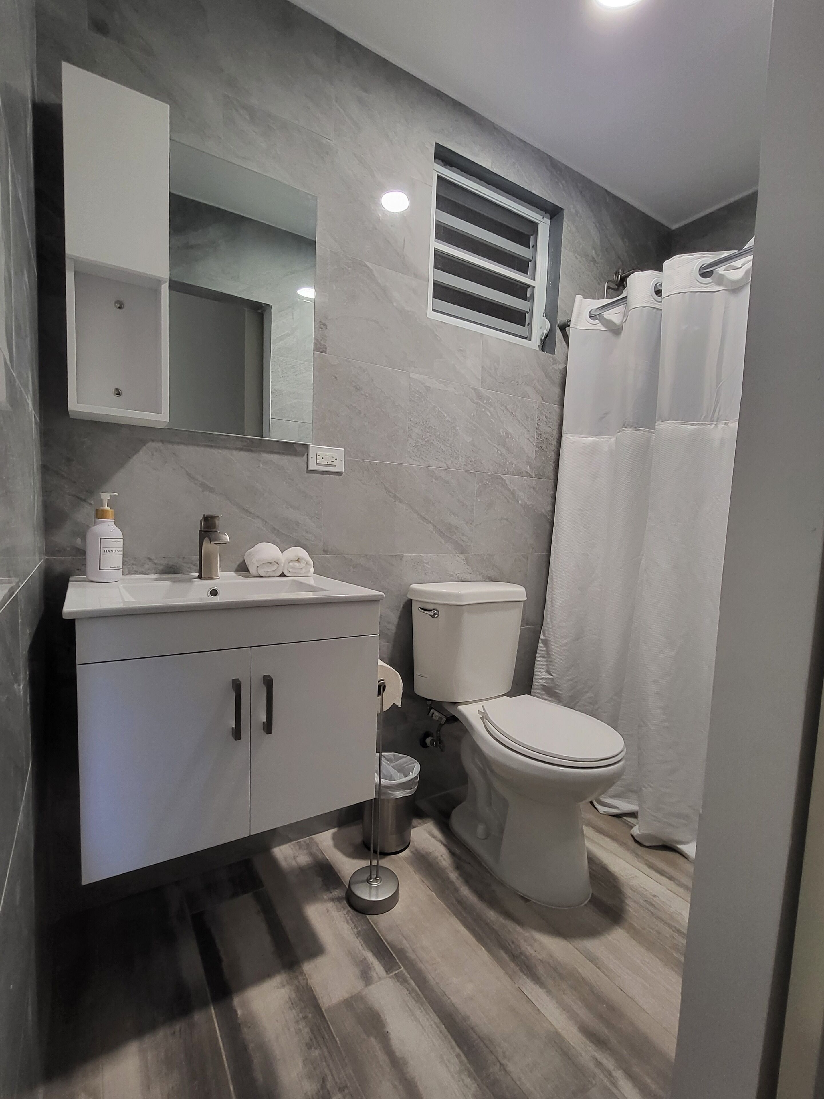 A modern bathroom with a marble floor, a white sink with a mirror above it, a toilet, and a shower curtain.