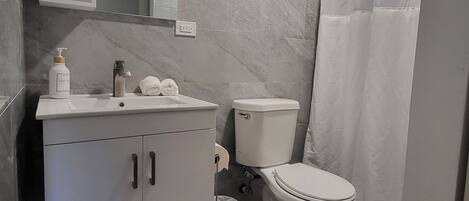 A modern bathroom with a marble floor, a white sink with a mirror above it, a toilet, and a shower curtain.
