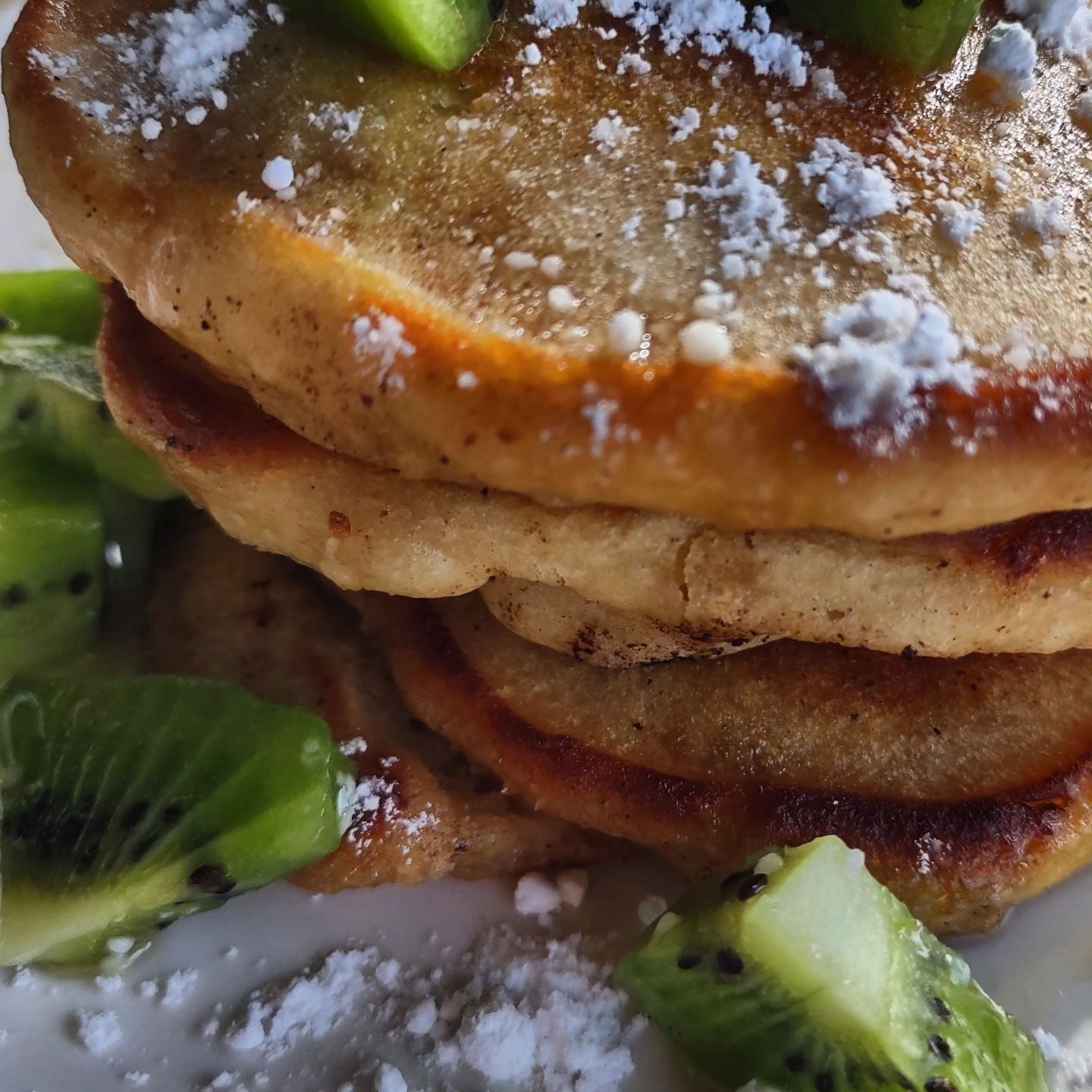 A stack of pancakes with kiwi slices and powdered sugar.