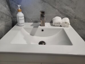 Un lavabo de salle de bain avec un flacon de savon liquide et deux serviettes enroulées.