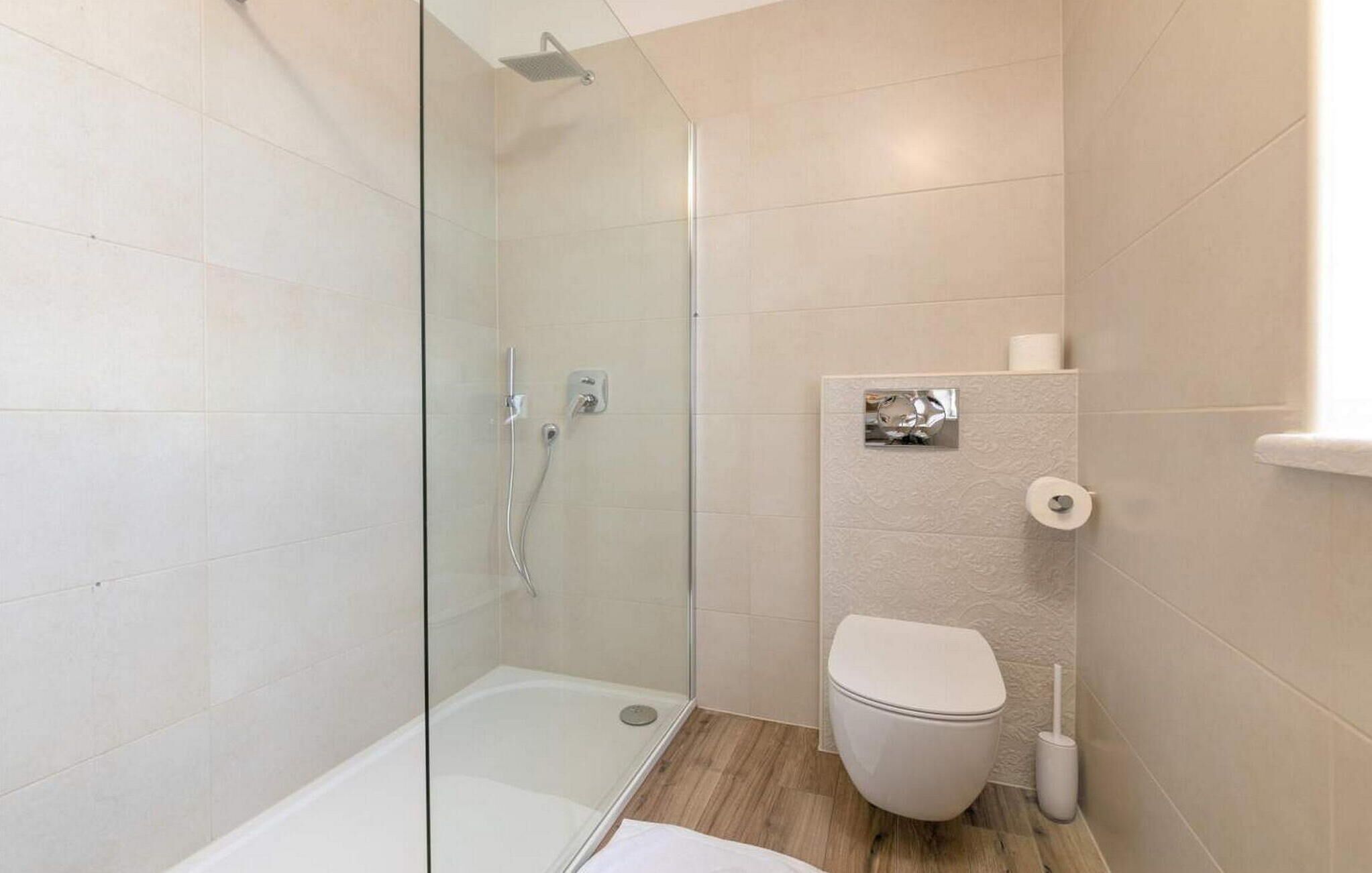Une salle de bain moderne avec une douche à parois de verre, des toilettes blanches et un plancher en bois.