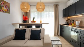 A modern kitchen with dark cabinets, a built-in oven, and a dining area with a sofa and two black cushions.