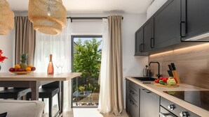 A modern kitchen with a wooden countertop, a built-in oven, and a sink. There is a dining area with a table and chairs, and a view of greenery outside.
