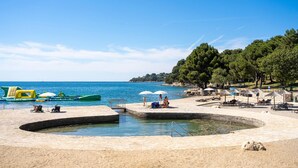 A beach with a swimming pool, umbrellas, and lounge chairs.