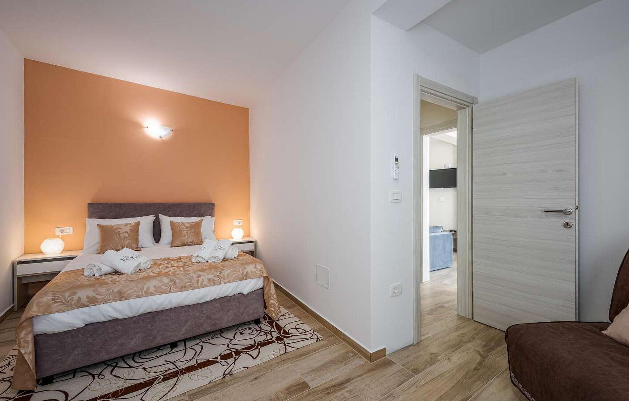 Een slaapkamer met een bed, nachtkastjes, een wandlamp, een deur en een gang die naar een andere kamer leidt.