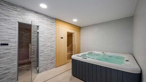 A modern bathroom with a walk-in shower, a wooden door, and a hot tub.