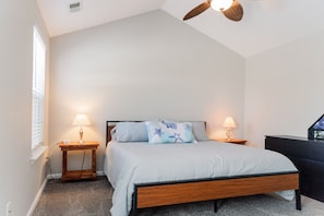 Un dormitorio con cama, dos mesitas de noche con lámparas, un ventilador de techo y un aparador.