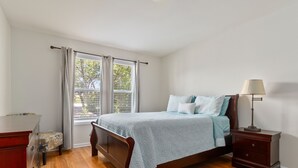 Une chambre à coucher avec un lit, une table de chevet, une commode et une fenêtre avec des rideaux.