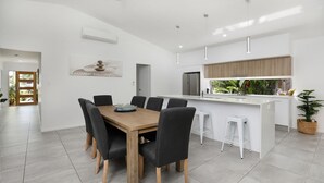 A modern kitchen with a central island, white cabinetry, and a dining area with a wooden table and chairs. - Seaside heated pool (Palm Cove)