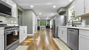 Una cocina moderna con electrodomésticos de acero inoxidable, armarios blancos y piso de madera.