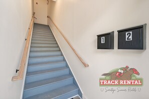 A staircase with blue steps, wooden handrails, and mailboxes labeled '1' and '2' on the wall.