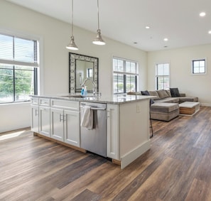 A modern kitchen with a central island, pendant lighting, and a view to the living area.